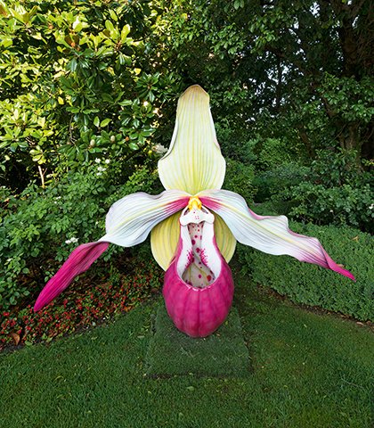 Scultura floreale monumentale a forma di orchidea di Marc Quinn, collocata nel giardino tra siepi e alberi