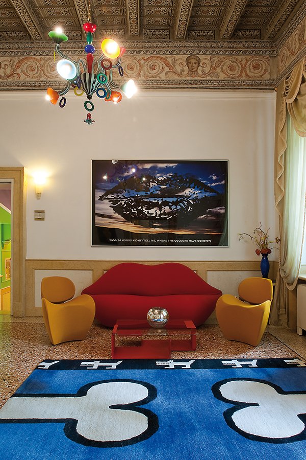 Interno artistico con divano rosso a forma di labbra e tappeto blu, sotto un'opera di Vanessa Beecroft esposta al Byblos