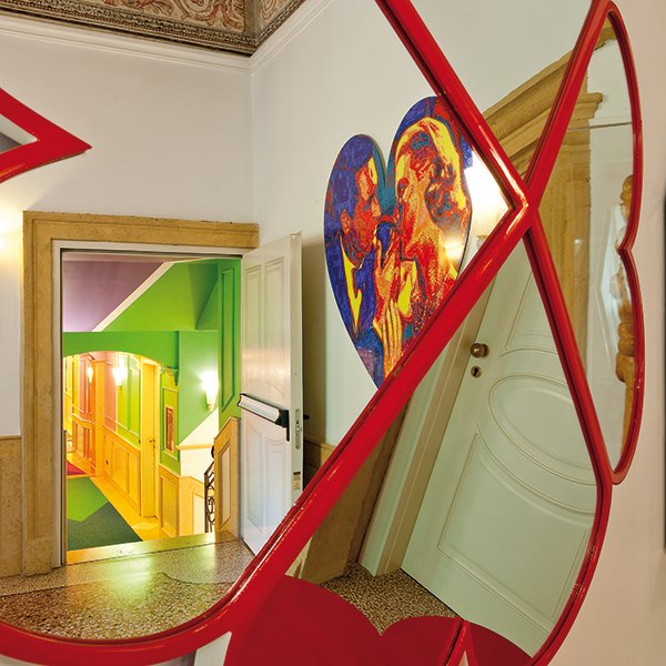 Ingresso con pareti verdi e specchio decorativo rosso che riflette un’opera di Pierre et Gilles al Byblos Art Hotel